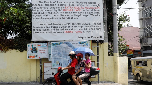A motorist drives a motorcycle past a banner denouncing the Bonnet Gang, a group allegedly nvolved in drug related killings