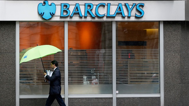  man shelters under umbrellas as he walks past a Barclays branch in central London
