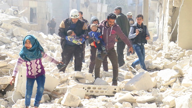 People and a civil defence personnel carry children at a damaged site after an air strike in Idlib