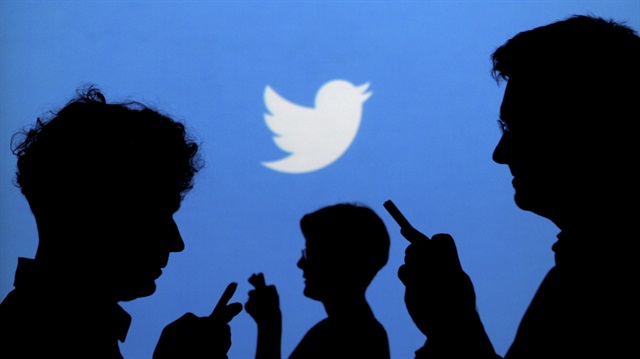 People holding mobile phones are silhouetted against a backdrop showing the Twitter logo