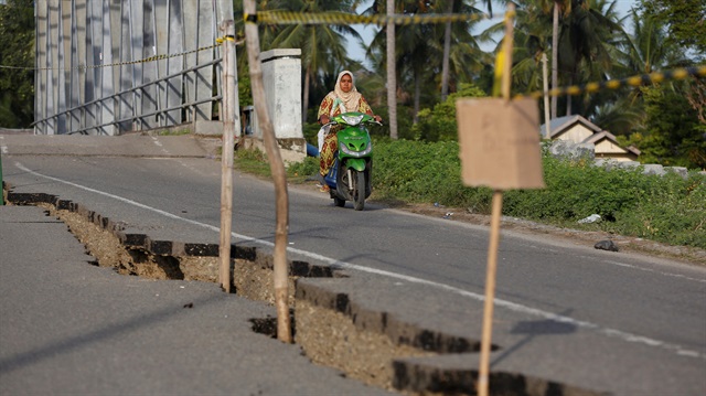 A woman drives her motorcycle past a section of road damaged following a strong earthquake in İndonesia