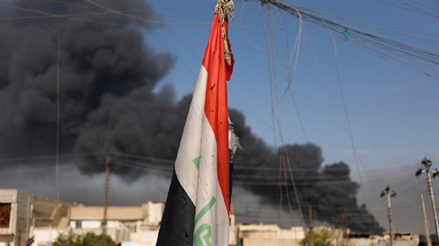 An Iraqi flag is shown as smoke rises in the background 