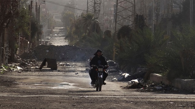 Men ride a motorbike along a deserted street filled with debris in Deir al-Zor