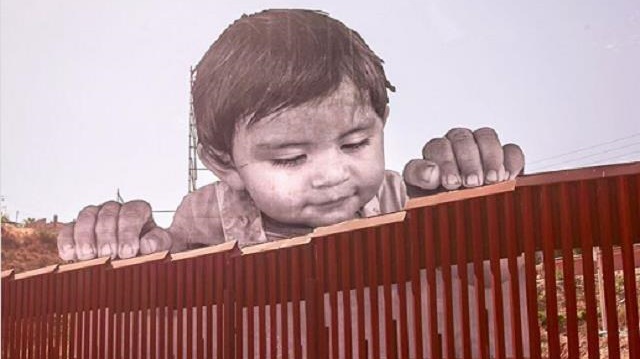 Sınırdaki portrede Meksikalı bir çocuk demir parmaklıklar ardından gülümserken görünüyor. 
