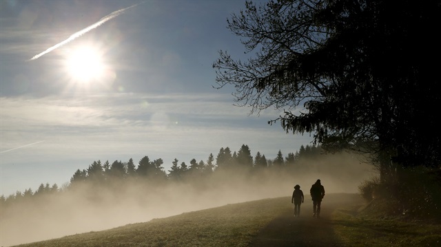 People walk along a forest as the sun shines over fog near Albis Pass mountain pass, Switzerland in this November 12, 2015 file picture.