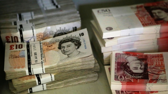 Wads of British Pound Sterling banknotes are stacked in piles