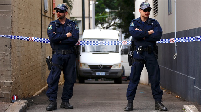 Police officers block a small alley where police vans are parked at a home being searched 