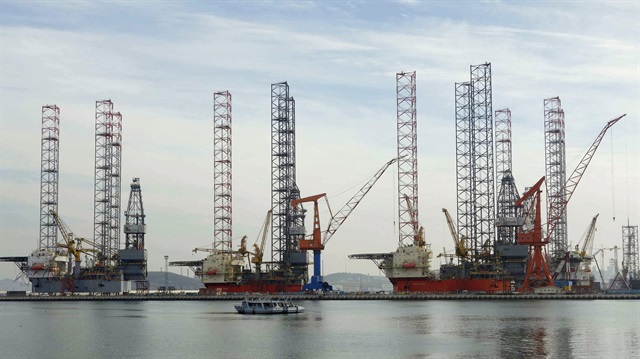 A boat travels past offshore drilling platforms under construction at a shipyard in China