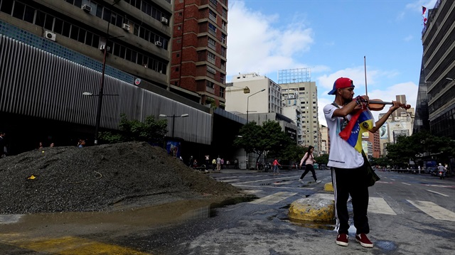 Venezuelan violinist Wuilly Arteaga plays the violin next to a pile of sand used by protesters to block the street during a protest against Venezuelan President Nicolas Maduro's government in Caracas, Venezuela.
