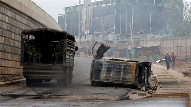 Kenyan anti-riot police drive past a burned car during clashes with supporters of Kenyan opposition 