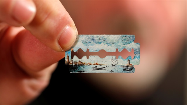 Turkish micro artist Hasan Kale displays one of his art work on a razor blade at his office