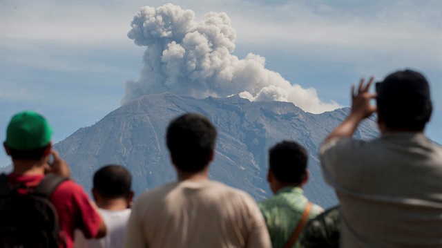 People watch as Mount Agung spews ash and smoke during an eruption f