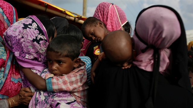 Rohingya refugees hold their children as they line up for a food supply distribution