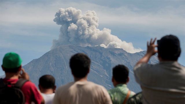 People watch as Mount Agung spews ash and smoke during an eruption 
