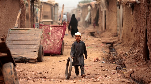 A boy plays with a tyre on an a street in an Afghan refugee camp in Islamabad, Pakistan