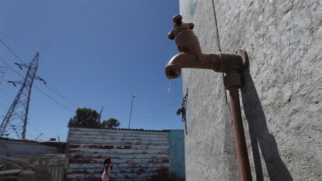 Residents walk past a leaking communal tap in Khayelitsha township, near Cape Town