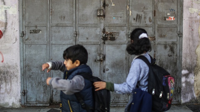 Palestinian children pass by in front of a shop, which took down the shutters for a day due to the recession on economic conditions and humanitarian crisis caused by Israel's blockade, in Gaza City, Gaza on February 20, 2018.