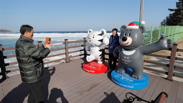 A man poses with the 2018 Pyeongchang Winter Olympics and Paralympics mascots Soohorang and Bandabi at the beach in Goseong