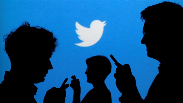 File Photo: People holding mobile phones are silhouetted against a backdrop projected with the Twitter logo in Warsaw