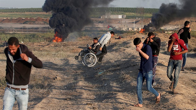 A wheelchair-bound Palestinian photographer is helped, as others react from tear gas