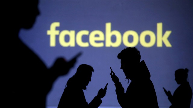 Silhouettes of mobile users are seen next to a screen projection of Facebook 