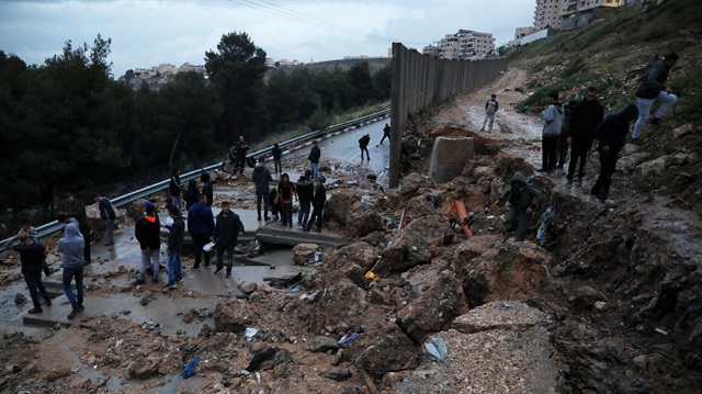 Palestinians stand next to a collapsed part of the Israeli barrier, following heavy weather, near the refugee camp of Shuafat in East Jerusalem, April 26, 2018. 