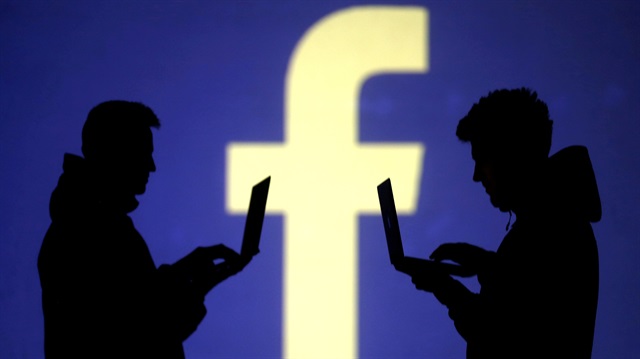 File Photo: Silhouettes of laptop users are seen next to a screen projection of Facebook 