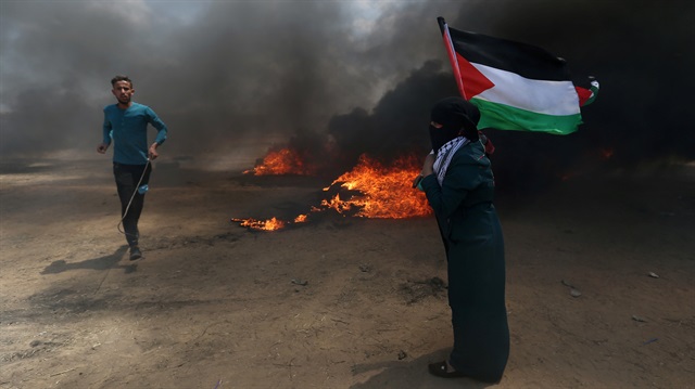 A woman holds a Palestinian flag as a demonstrator runs during a protest against U.S. embassy move to Jerusalem and ahead of the 70th anniversary of Nakba, at the Israel-Gaza border in the southern Gaza Strip May 14, 2018.