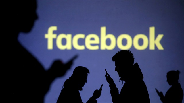  Silhouettes of mobile users are seen next to a screen projection of Facebook 