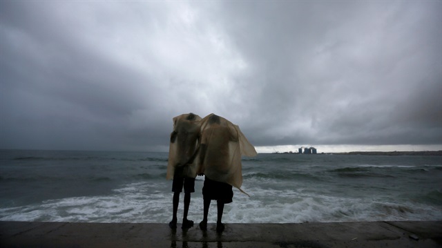 Two men use a plastic sheet to protect themselves from heavy monsoon rain as they stand by the sea in Colombo, Sri Lanka May 17, 2018. 