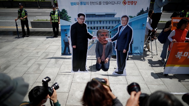 A man wearing a mask of U.S. President Donald Trump kneels down between cutouts of North Korean leader Kim Jong Un and South Korean President Moon Jae-in during an anti-U.S. President Donald Trump rally near U.S. embassy in Seoul, South Korea, May 25, 2018. 
