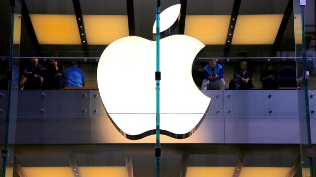 File Photo: A customer stands underneath an illuminated Apple logo as he looks out the window of the Apple store located in central Sydney