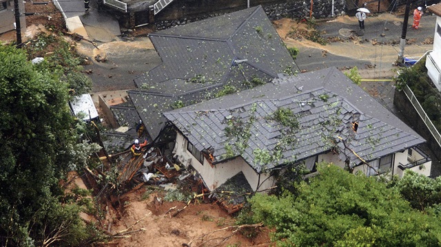 Rescue workers are seen next to houses damaged by a landslide following heavy rain in Kitakyushu, southwestern Japan.