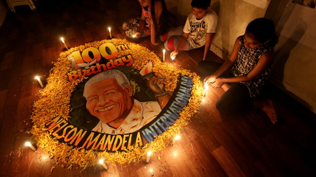Children light candles beside a painting commemorating South African revolutionary Nelson Mandela's 100th birth anniversary.