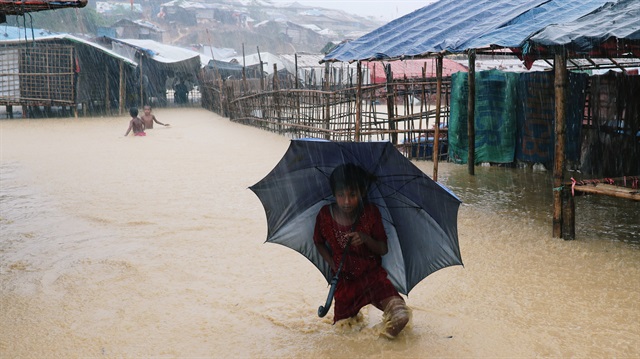 A Rohingya refugee girl walks along the water with umbrella