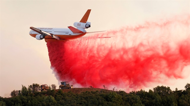 A DC-10 air tanker drops fire retardant along the crest of a hill to protect the two bulldozers 