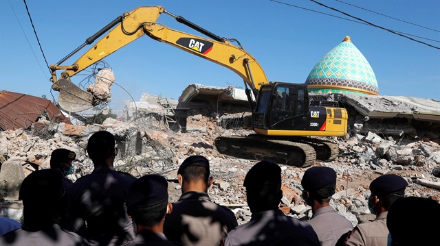 Policemen stand as heavy equipment move debris for try to find people trapped inside a mosque after an earthquake hit on Sunday in Pemenang, Lombok Island, Indonesia.