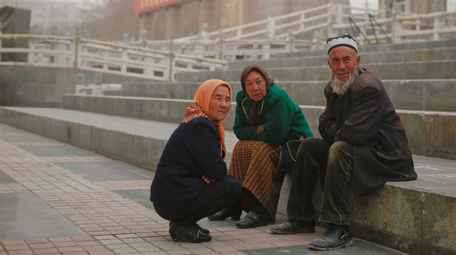 Ethnic Uighurs sit near a statue of China's late Chairman Mao Zedong in Kashgar, Xinjiang 