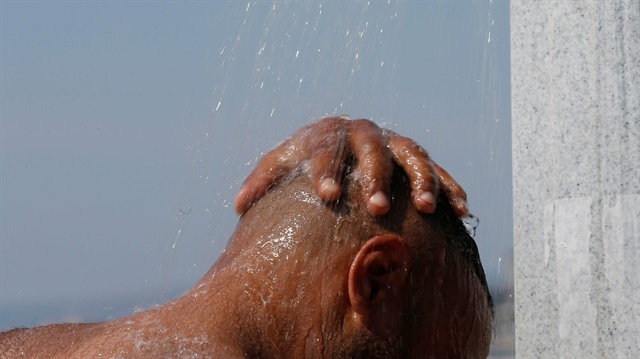 A man cools off under a beach shower as a heatwave with high temperatures 