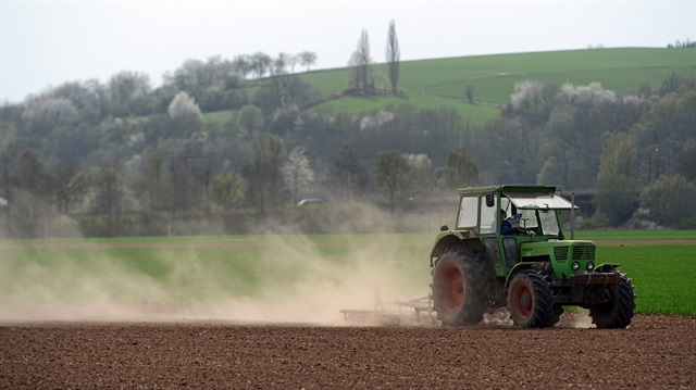 A tractor harrowing a field creates a trail of dust near Jestaedt, Germany