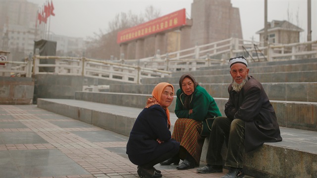 Ethnic Uighurs sit near a statue of China's late Chairman Mao Zedong