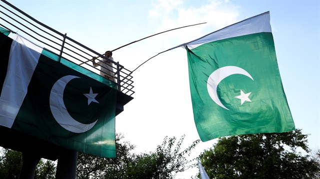 A boy uses a bamboo stick to adjust national flags at an overhead bridge 