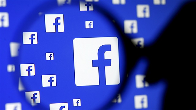 A man poses with a magnifier in front of a Facebook logo