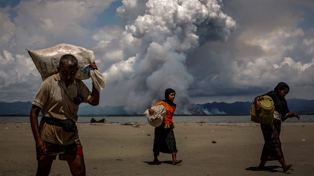 Smoke is seen on the Myanmar border as Rohingya refugees walk on the shore after crossing the Bangladesh-Myanmar border by boat through the Bay of Bengal, in Shah Porir Dwip, Bangladesh September 11, 2017. 