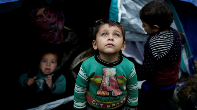  Syrian refugee boy stands in front of his family tent at a makeshift camp