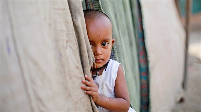 A girl from the Rohingya community stands outside her family's shack