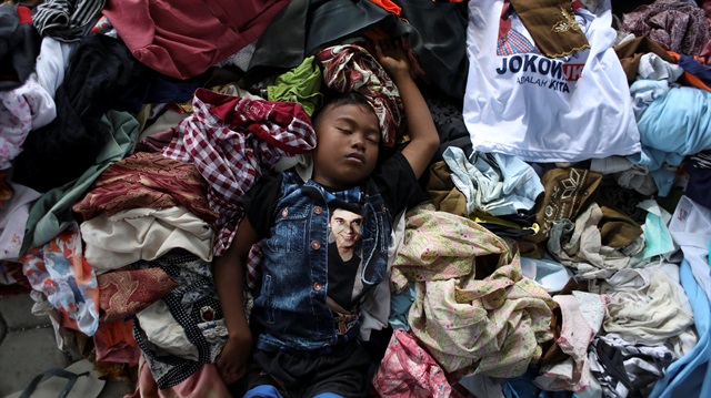 A boy sleeps over a pile of recycled clothes at a camp for displaced victims of the earthquake and tsunami in Palu, Central Sulawesi, Indonesia, October 9, 2018.