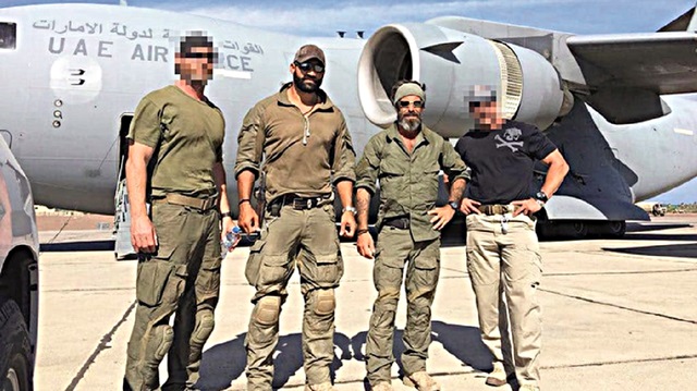 Standing in front of a UAE military plane are Gilmore (middle left), Golan (middle right), and two soldiers on their mercenary team.