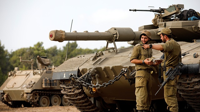 Israeli soldiers speak next to a tank as military armoured vehicles gather in an open area near Israel's border with the Gaza Strip 