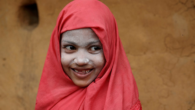 A Rohingya refugee girl smiles as she applies Thanaka paste in the Kutupalong camp in Cox's Bazar
